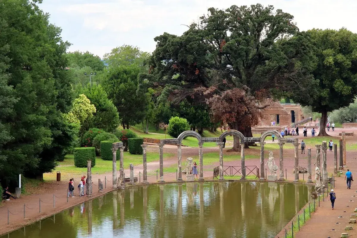 Vestiges antiques et étang reflétant le ciel à la Villa Adriana de Tivoli. Des colonnes romaines bordent l'eau, entourées de verdure luxuriante.