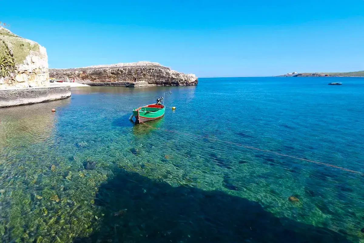 Un bateau vert et rouge flotte dans les eaux cristallines de Polignano a Mare, dans les Pouilles. Le soleil brille sur la mer Adriatique.