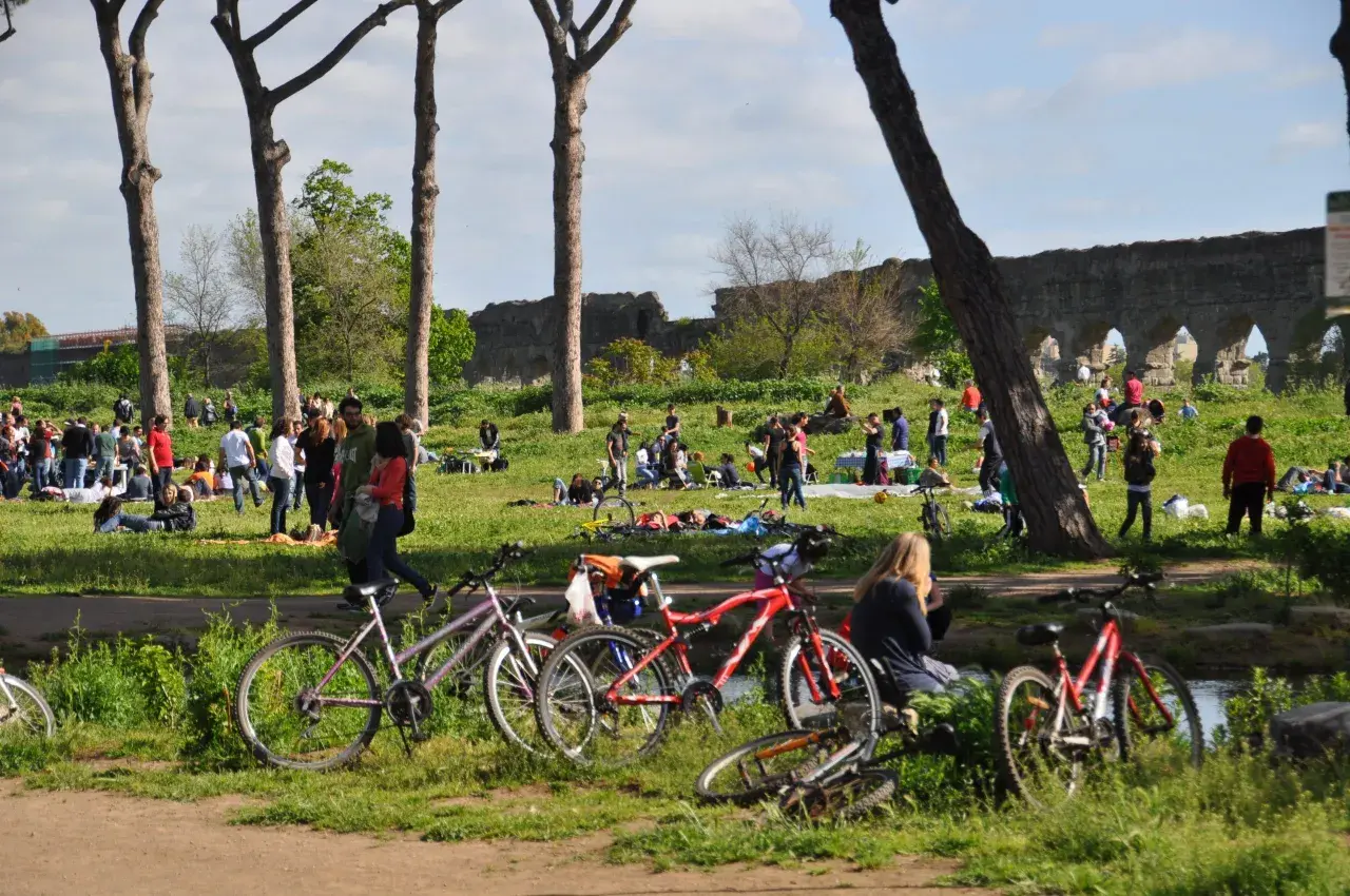 Des vélos garés près d'un parc à Rome, où des gens profitent du soleil et des ruines antiques.