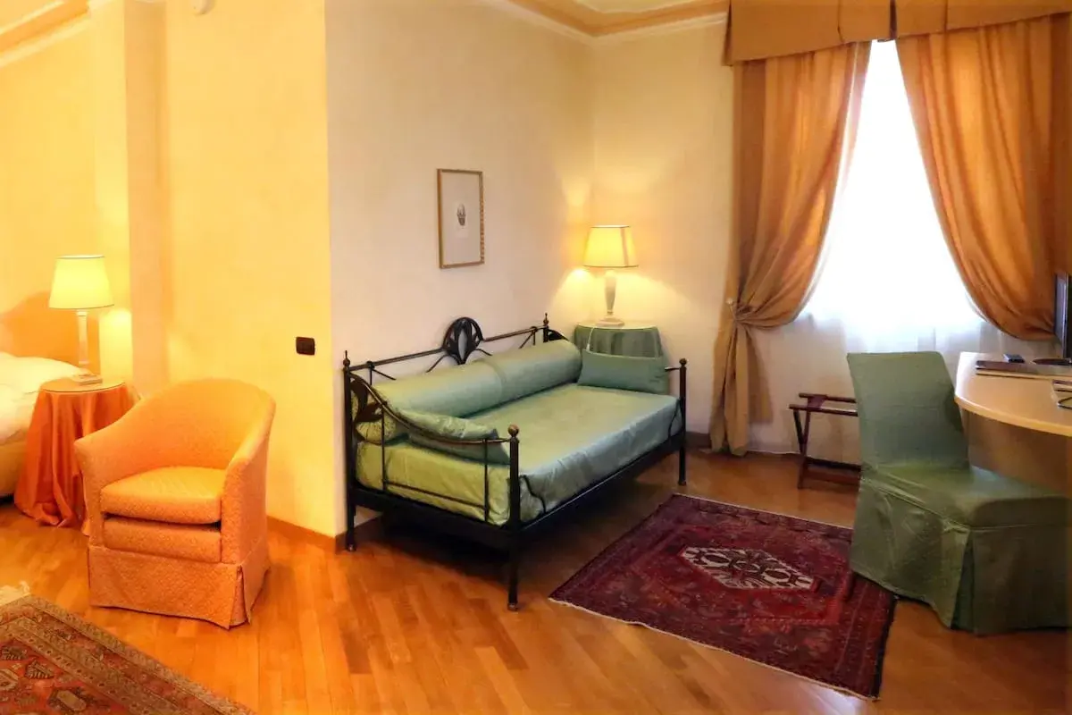 Chambre confortable dans un des hôtels de Castiglione Tinella, avec un lit de repos vert, un fauteuil orange et des rideaux dorés.