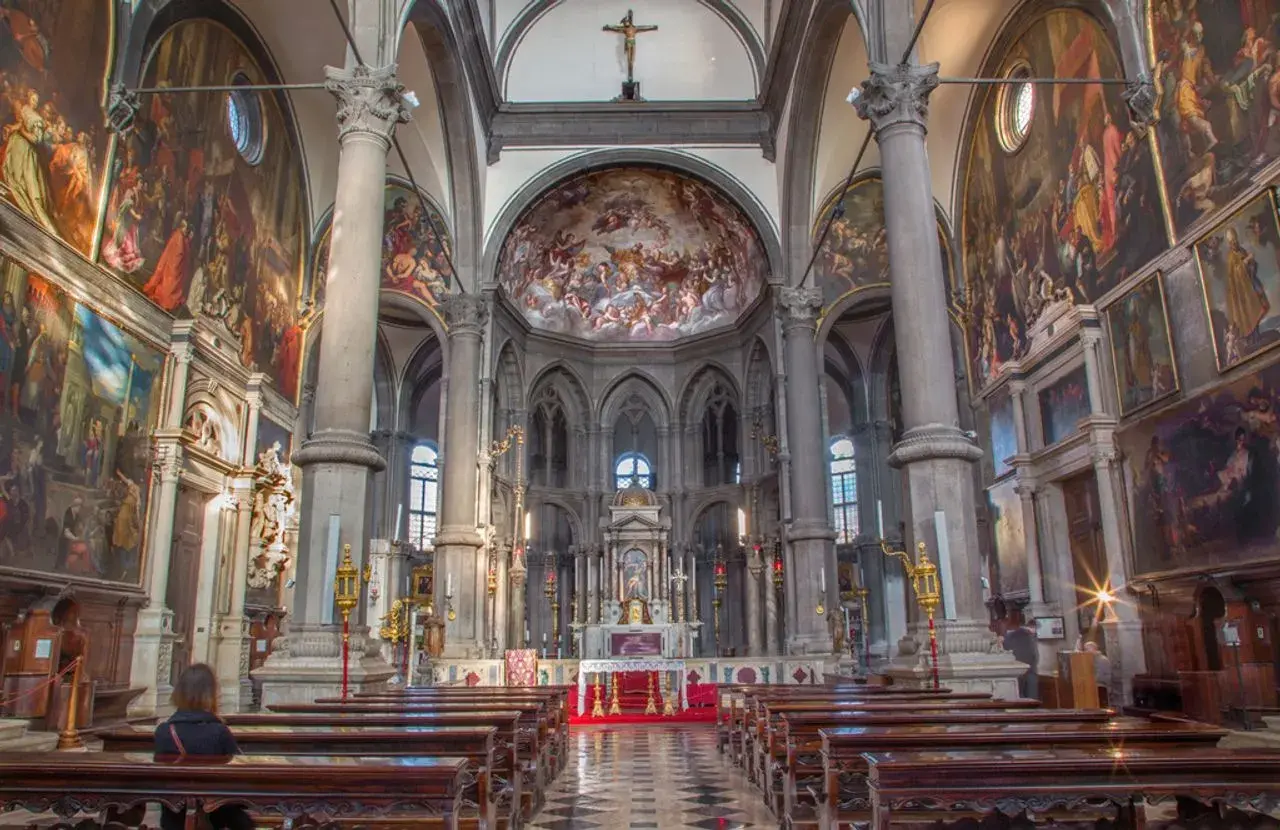 Intérieur de San Zaccaria à Venise, avec des fresques grandioses, des colonnes imposantes et des bancs en bois.