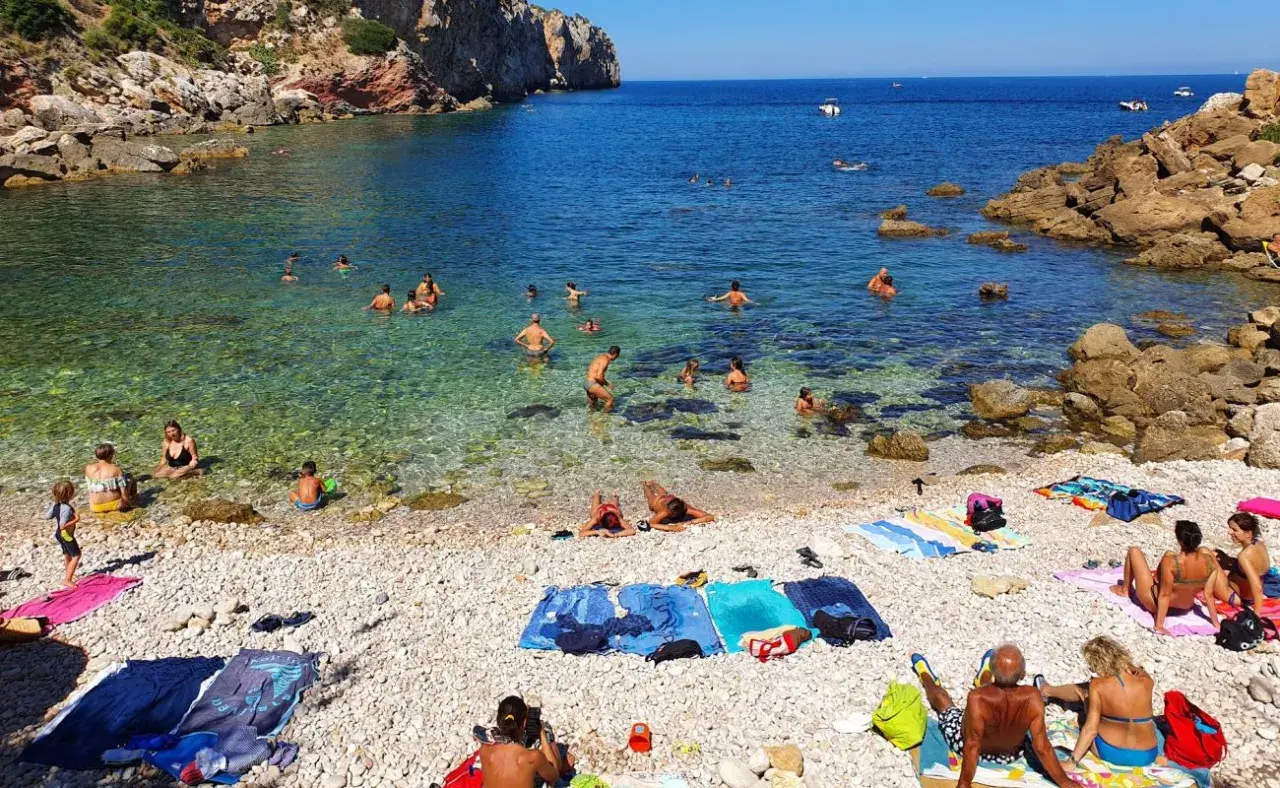 Plage de galets à Terrasini, Sicile. Des baigneurs profitent de l'eau cristalline sous un soleil radieux.