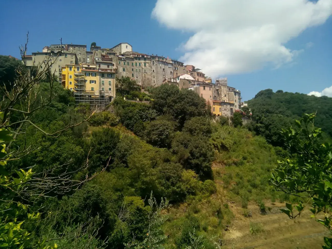 Village d'Ameglia perché sur une colline verdoyante, avec des maisons colorées et un ciel bleu éclatant.