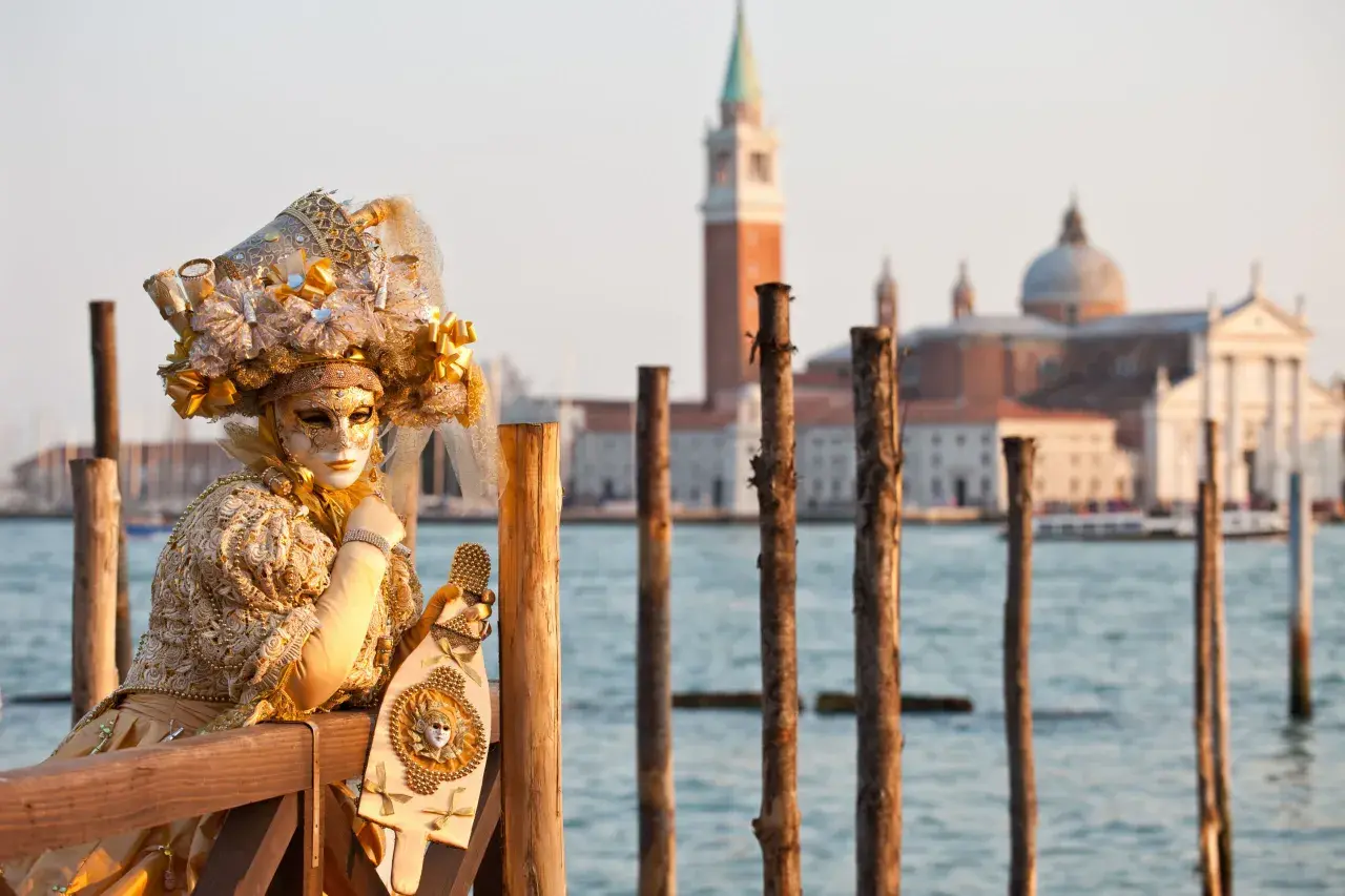 Une personne masquée et costumée, prête pour le carnaval, pose près de l'eau. Une belle image pour savoir quand aller à Venise.