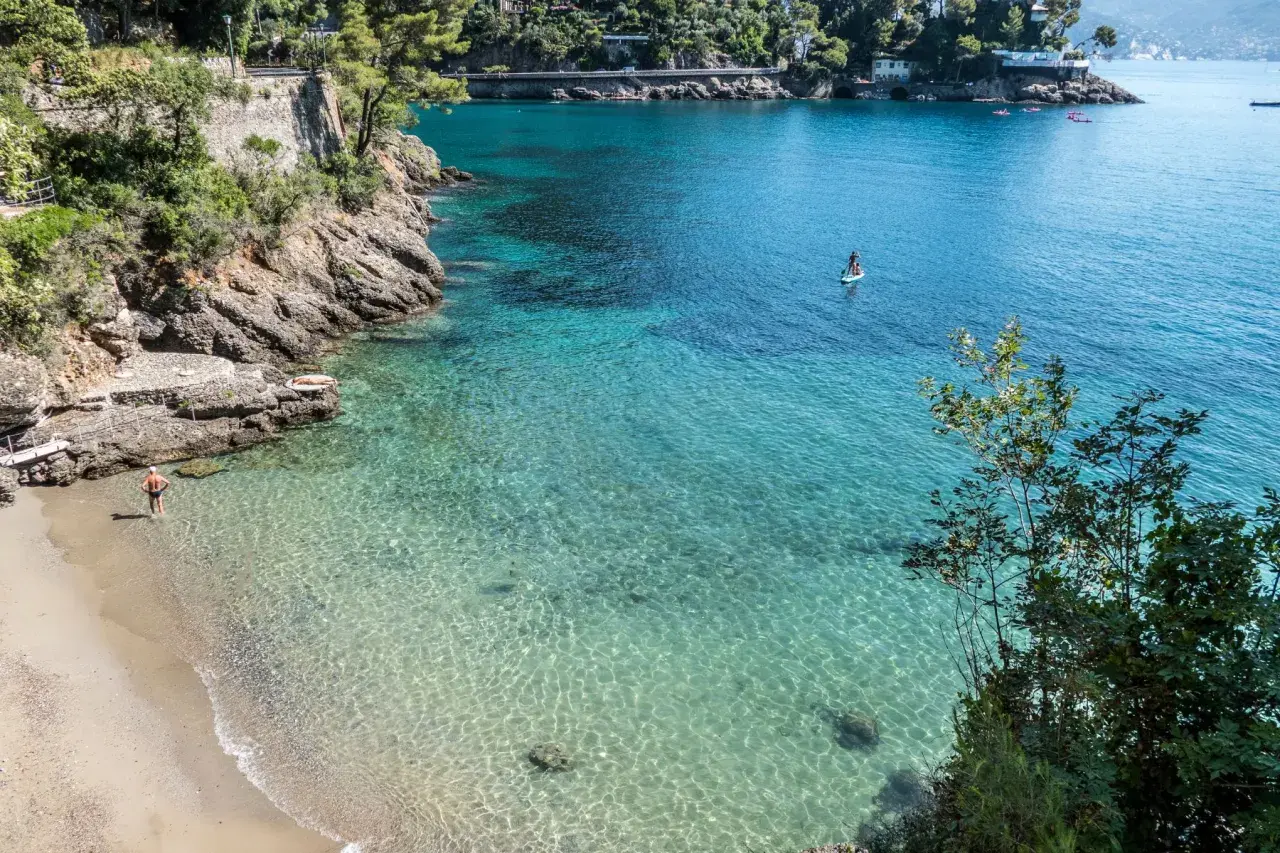 Un homme profite de ses vacances à Portofino, se baignant dans les eaux cristallines. Une personne fait du paddleboard au loin.