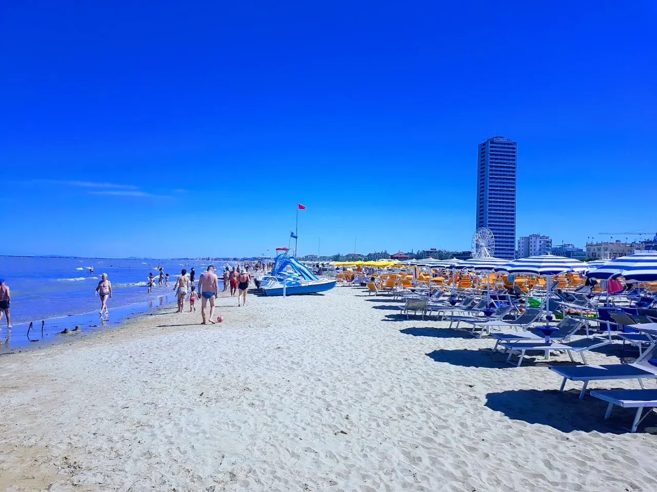 Plage animée à Cesenatico, Italie, avec des parasols rayés, des chaises longues et des baigneurs profitant du soleil sous un ciel bleu éclatant.