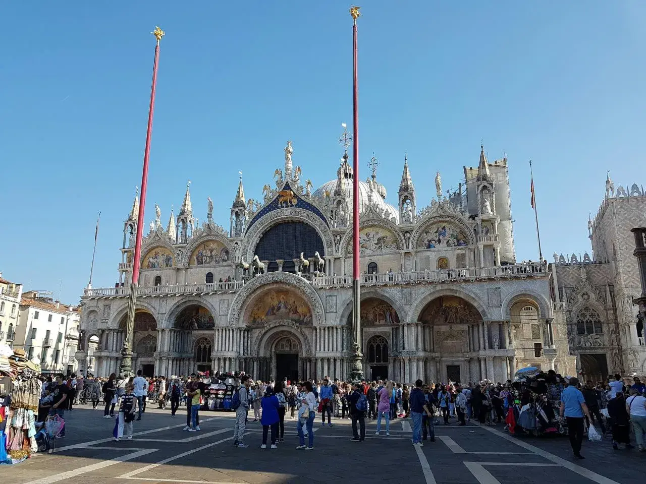 La place animée devant la magnifique église de Venise, avec ses dômes et ses mosaïques, sous un ciel bleu éclatant.