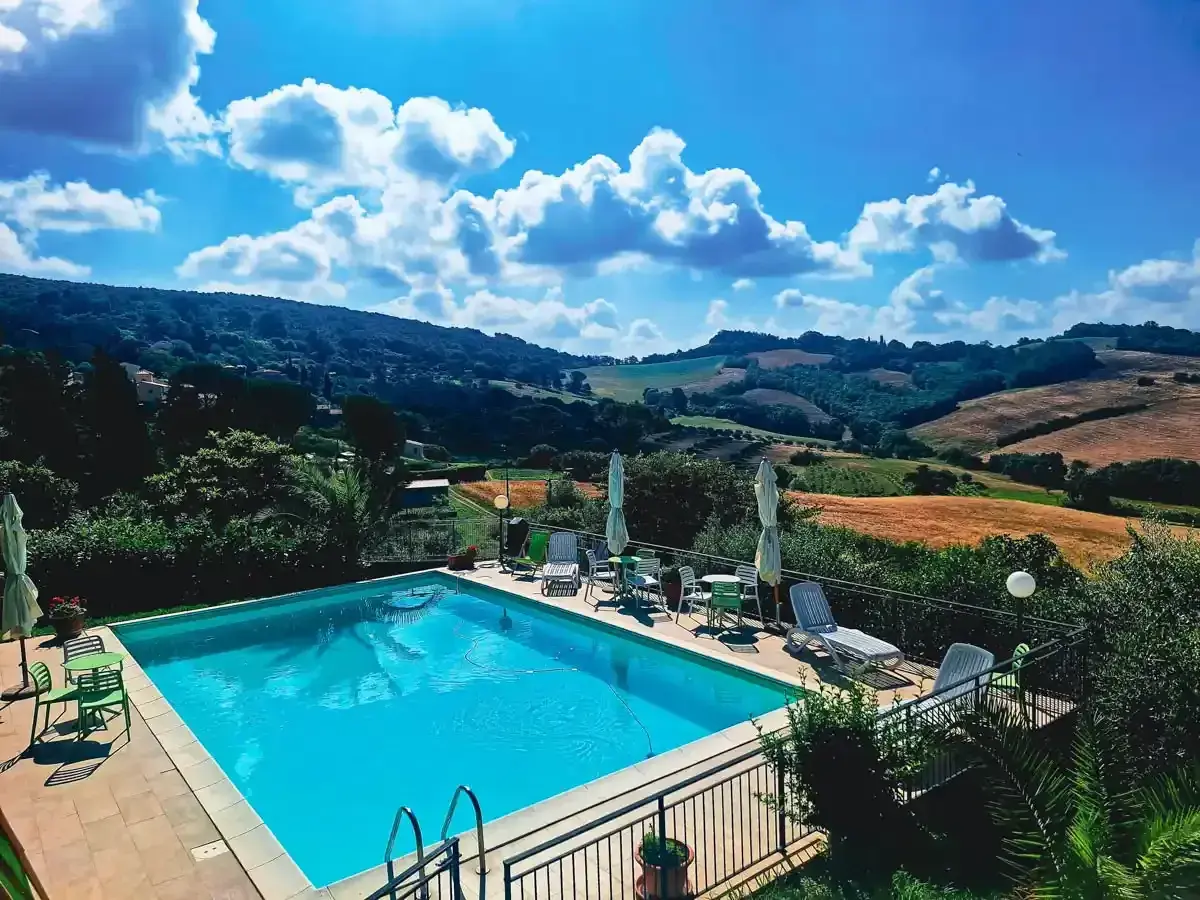 Piscine étincelante devant une **ferme toscane** pittoresque, avec des collines ondulantes et un ciel bleu éclatant.