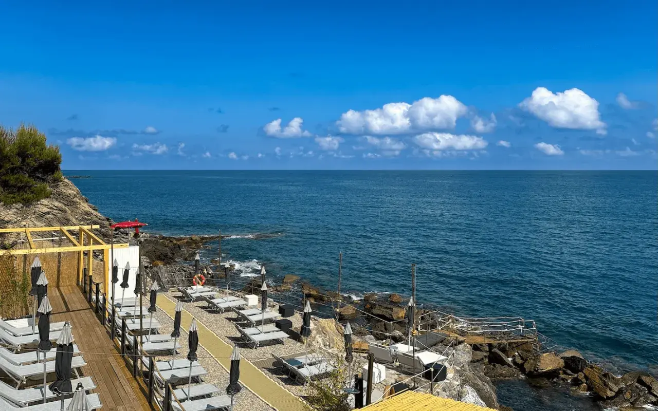 Plage aménagée à San Bartolomeo al Mare, avec chaises longues et parasols face à la mer bleue sous un ciel d'été.