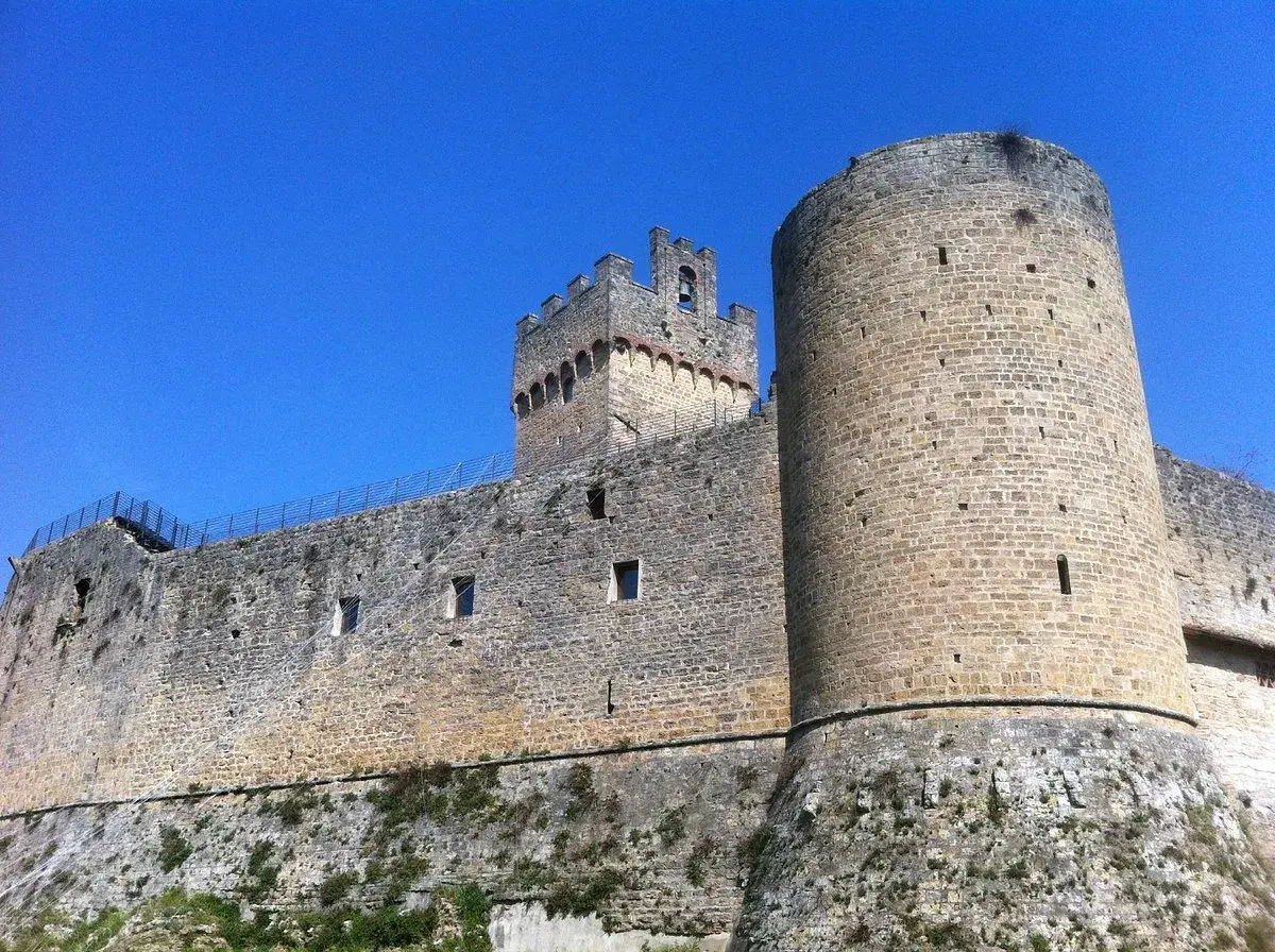 Château médiéval imposant à Poggibonsi, Italie, avec ses tours rondes et carrées sous un ciel bleu éclatant.
