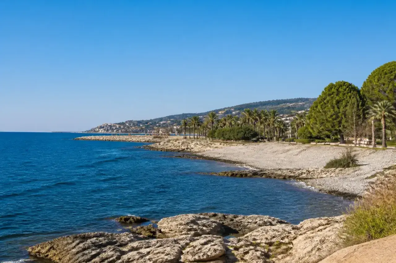 Côte rocheuse et mer bleue près d'une ville côtière en Italie, Imperia, avec des palmiers et des pins.