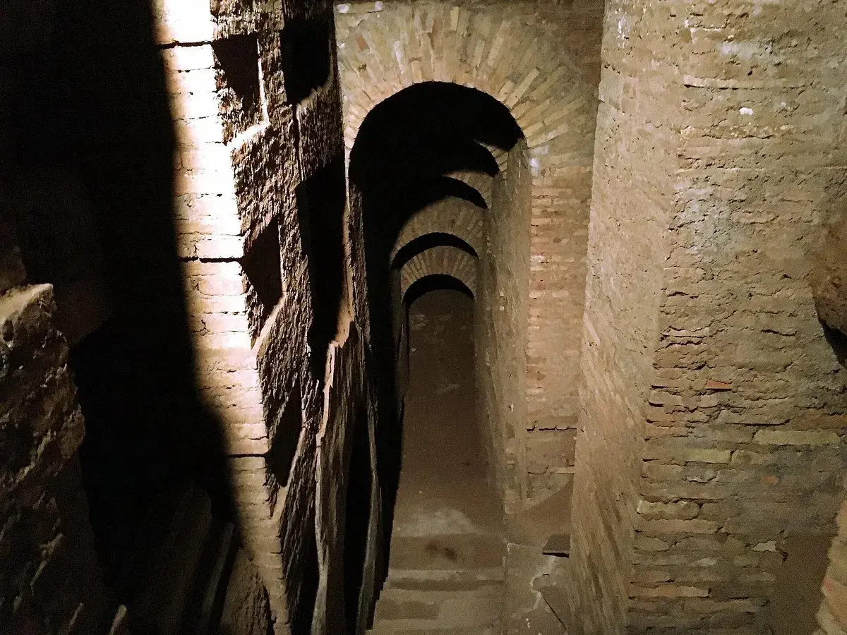 Passage voûté dans les catacombes de Rome, avec des niches creusées dans le mur de briques.