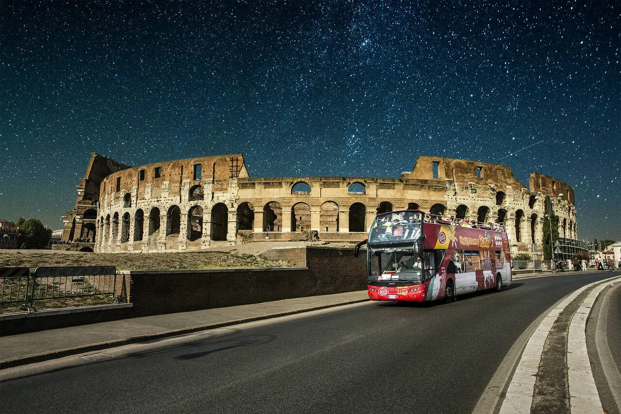 Un bus de nuit Rome passe devant le Colisée sous un ciel étoilé.
