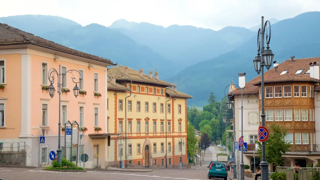 Vue d'une rue à Cavalese, Italie, avec des bâtiments colorés et des montagnes en arrière-plan.
