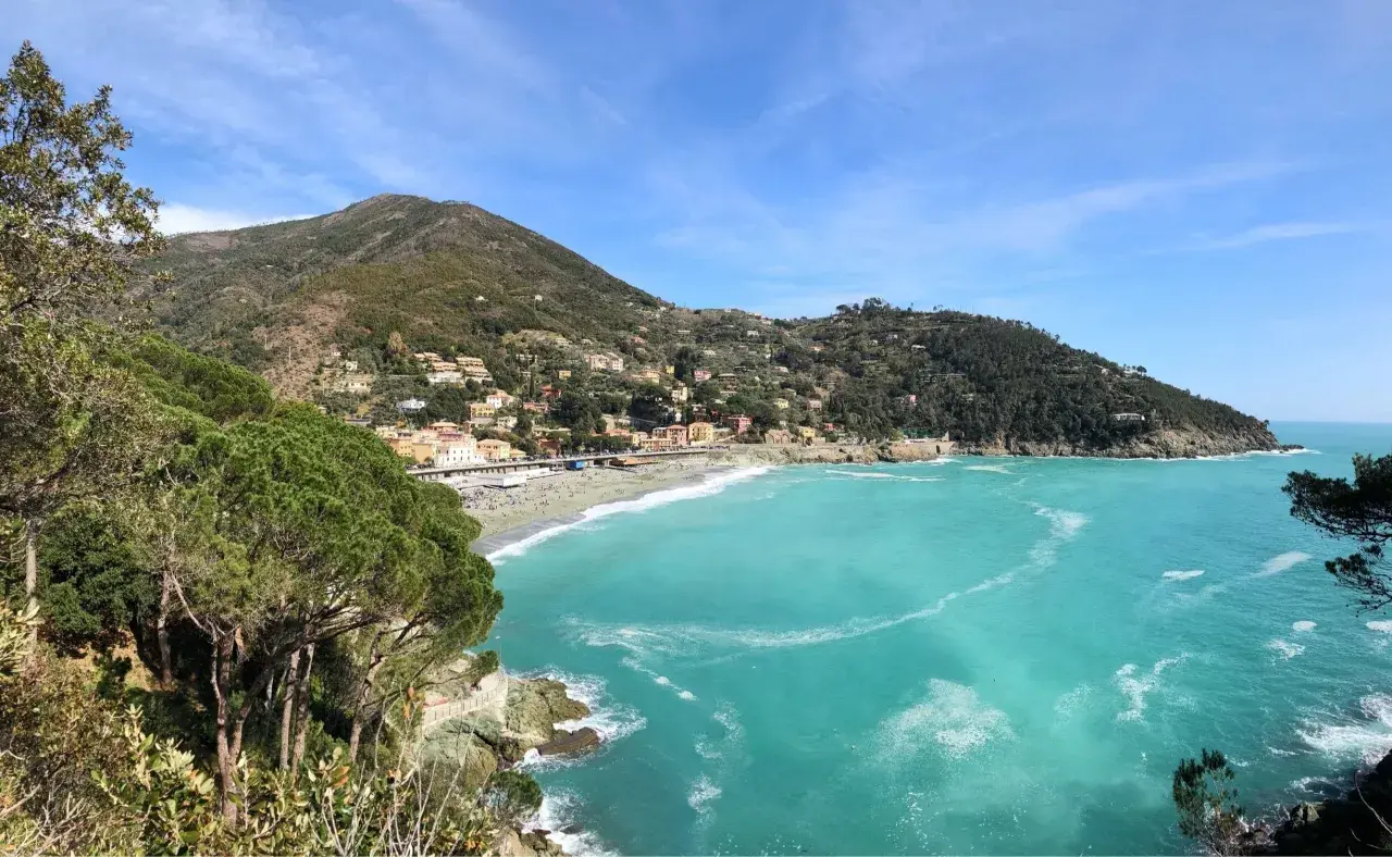 Vue panoramique de la baie de Bonassola en Italie, avec ses eaux turquoise, sa plage animée et ses collines verdoyantes couvertes de maisons.