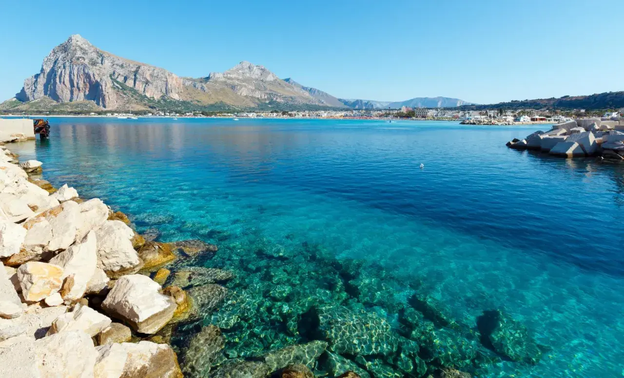 Vue sur la mer turquoise et les montagnes de Capo San Vito. Des rochers blancs bordent la côte.