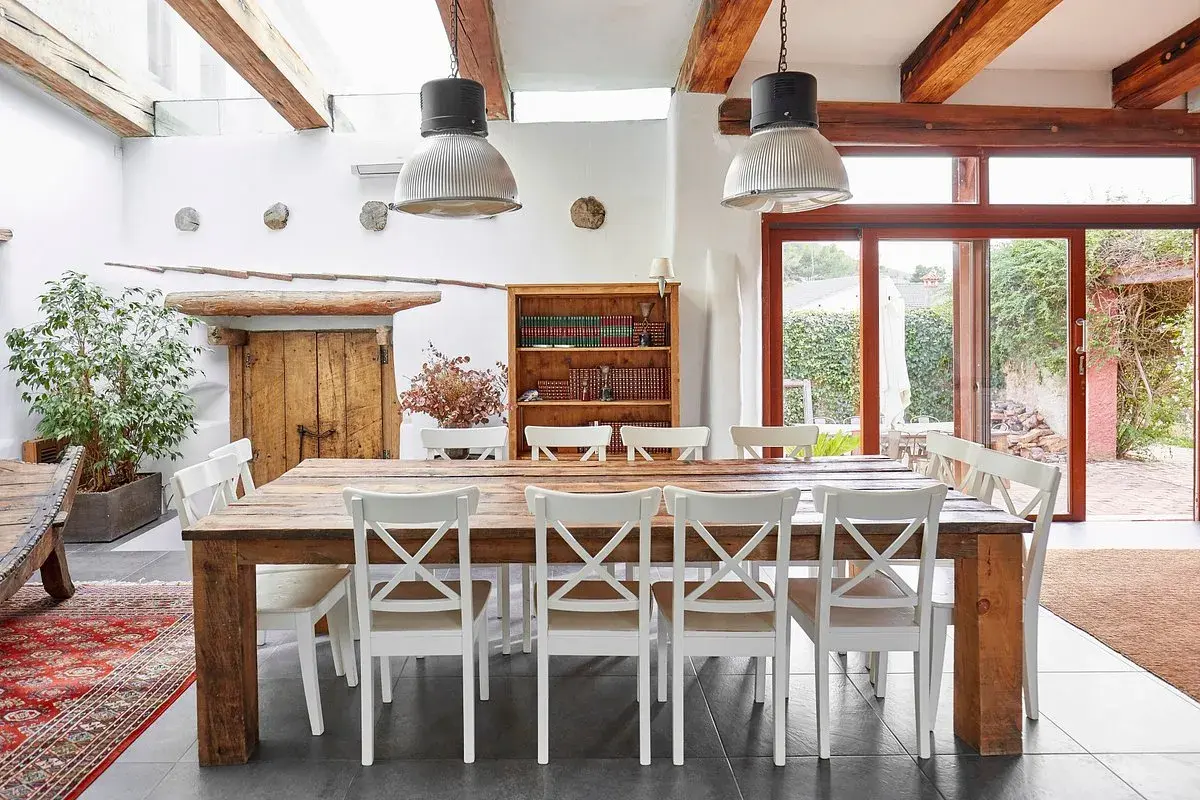 Salle à manger rustique d'un agriturismo en Ligurie, avec table en bois massif, chaises blanches et grande porte vitrée donnant sur le jardin.