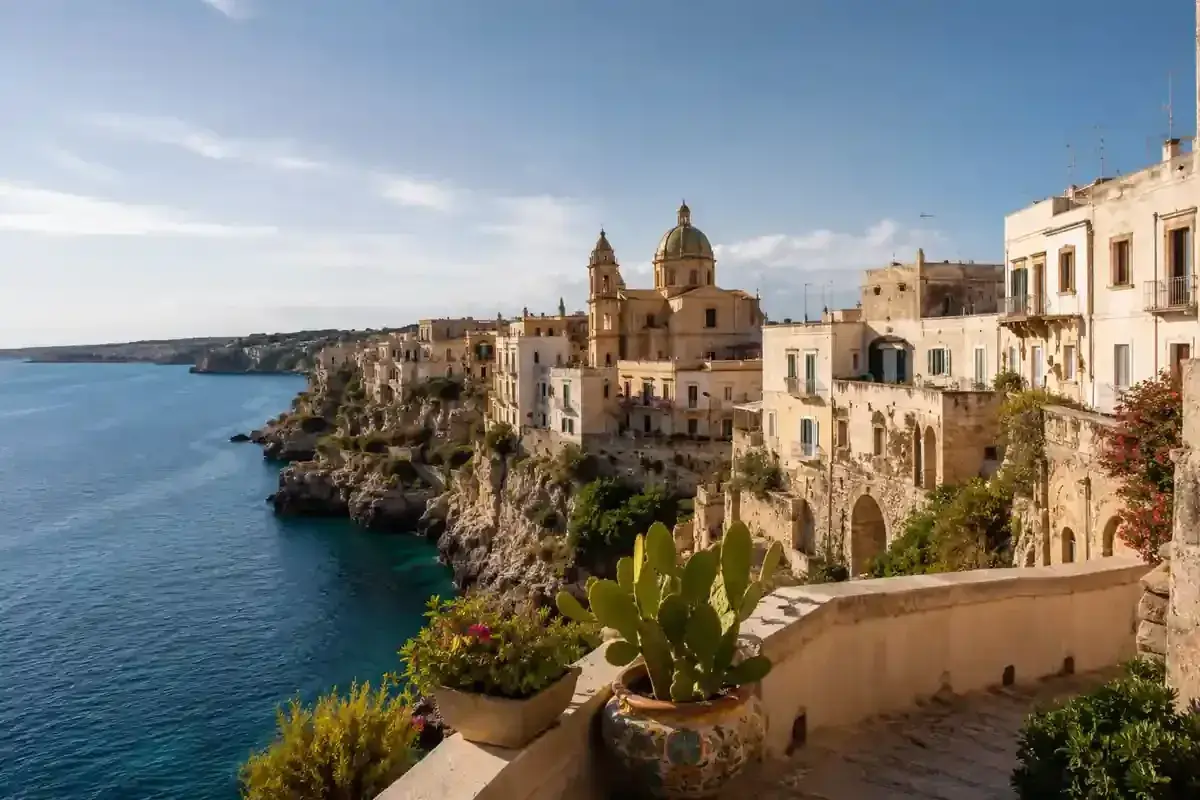 Vue d'une ville côtière italienne perchée sur une falaise, avec des maisons blanches et une église. Idéal pour une maison à louer en Italie.