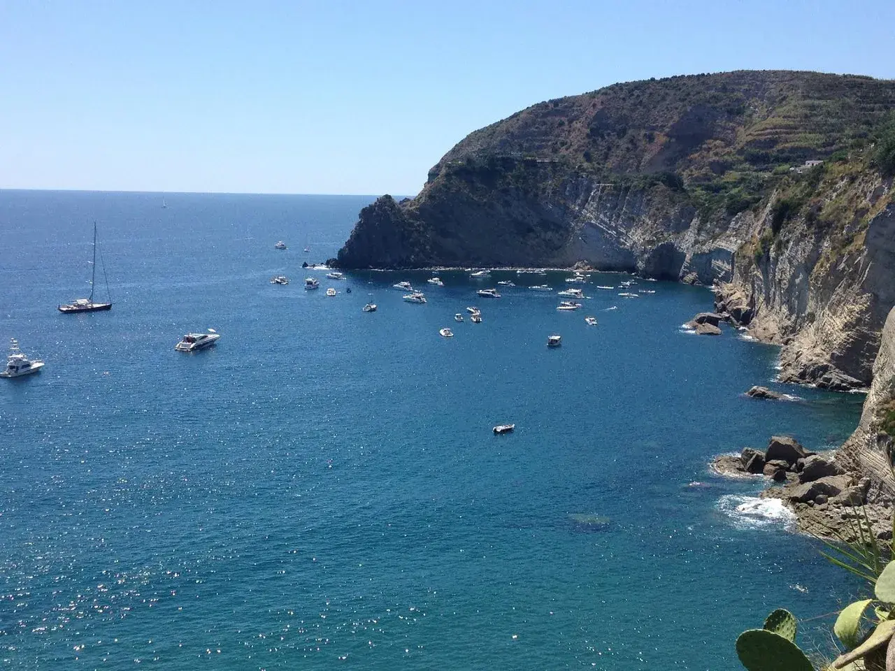 Baie de Sant'Angelo à Ischia, parsemée de bateaux sous un ciel bleu éclatant.
