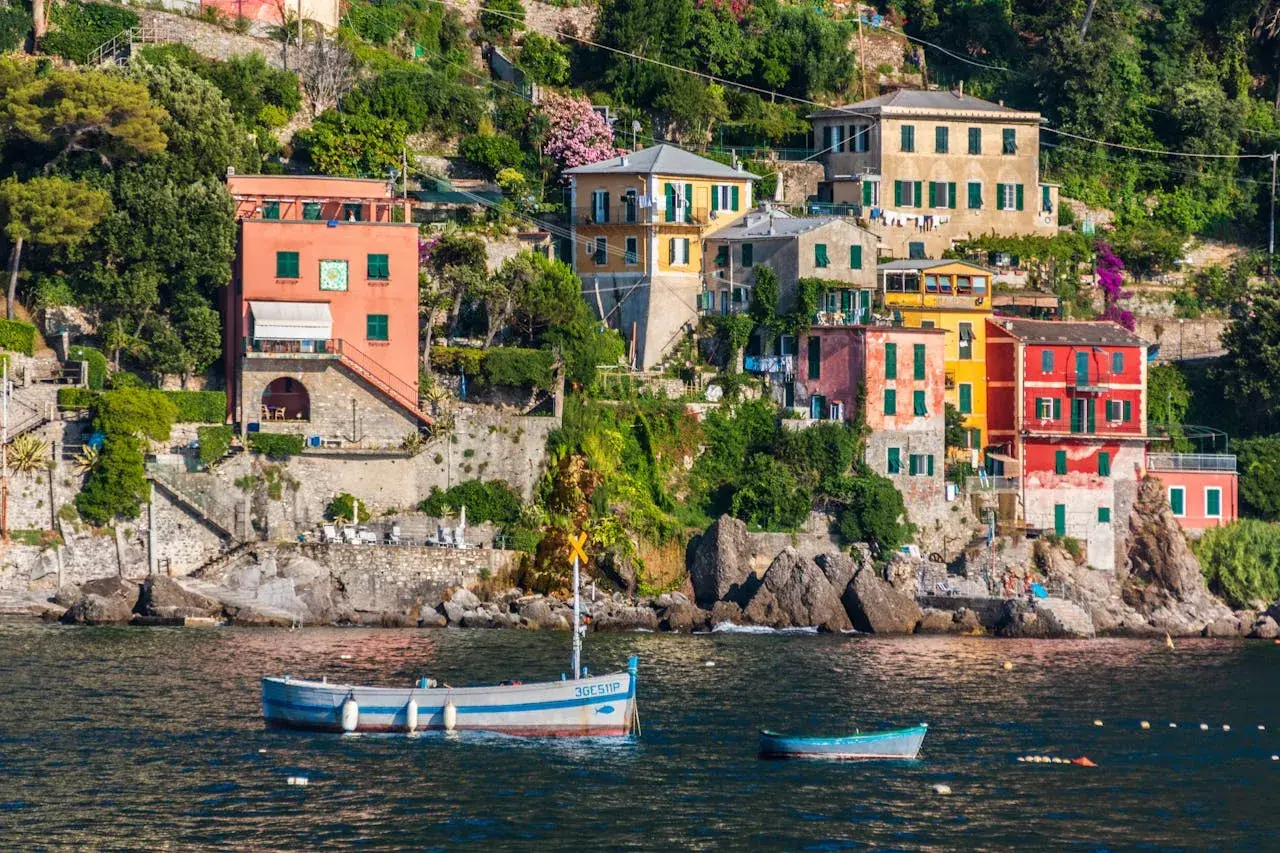 Des maisons colorées s'accrochent à la falaise sur la **riviera italienne où aller**. Des bateaux flottent paisiblement dans l'eau bleue.