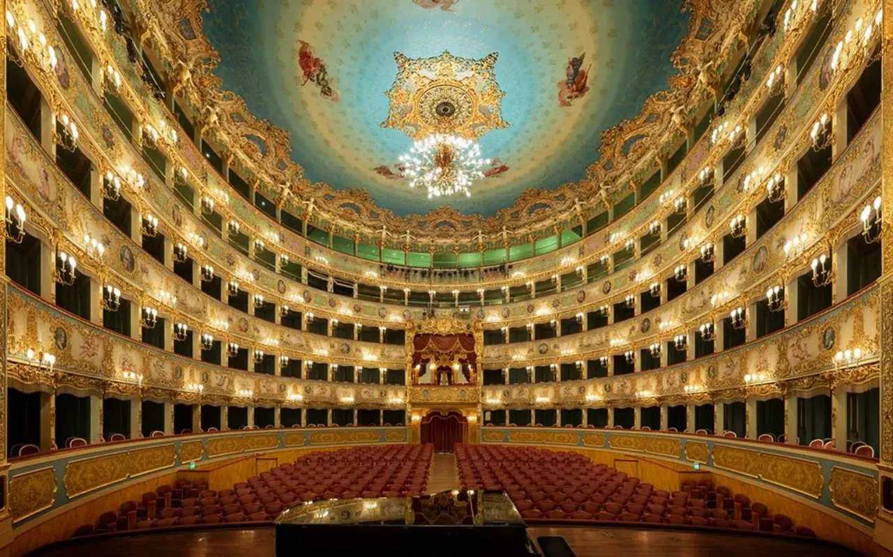 L'intérieur doré et orné du théâtre La Fenice, avec ses loges superposées, ses lustres étincelants et son plafond peint, prêt à accueillir un concert.
