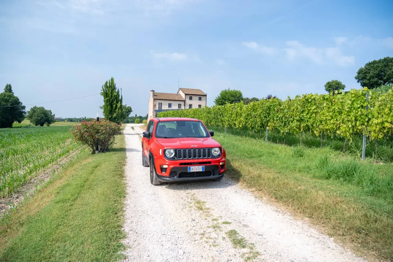 Une voiture rouge Jeep sur un chemin de gravier en Italie, près d'un vignoble. Le prix de cette voiture est très attractif.