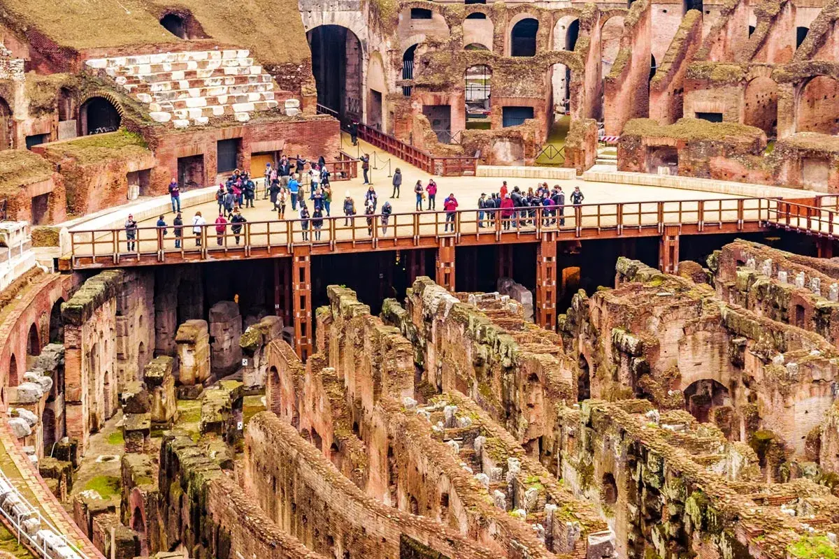Vue d'ensemble de l'arène du Colisée à Rome, avec des touristes sur une passerelle surplombant les ruines antiques.