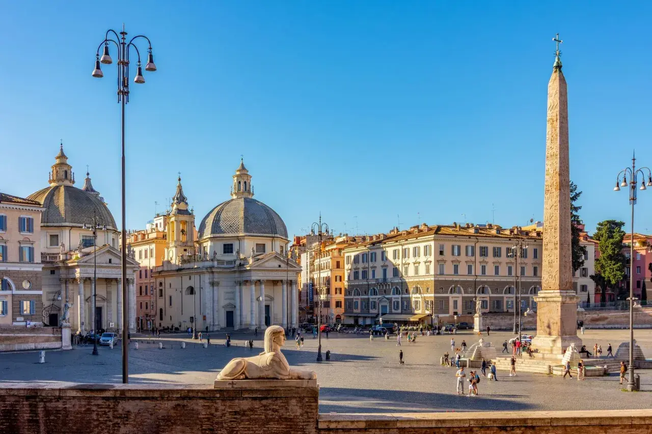 La Piazza del Popolo à Rome, avec ses églises jumelles, son obélisque et son sphinx, sous un ciel bleu éclatant.