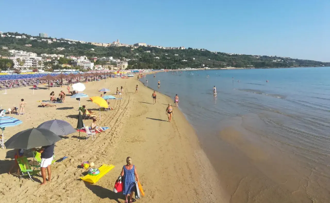Plage animée à Vasto, Italie, avec des parasols colorés, des baigneurs et une ville en arrière-plan.