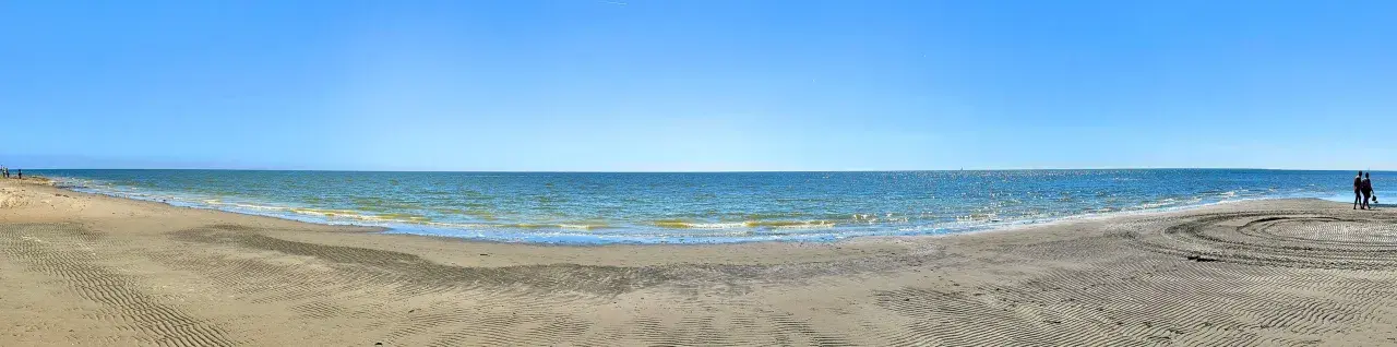 Vaste étendue de sable et de mer au Lido degli Estensi sous un ciel bleu clair. Des vagues douces caressent le rivage.