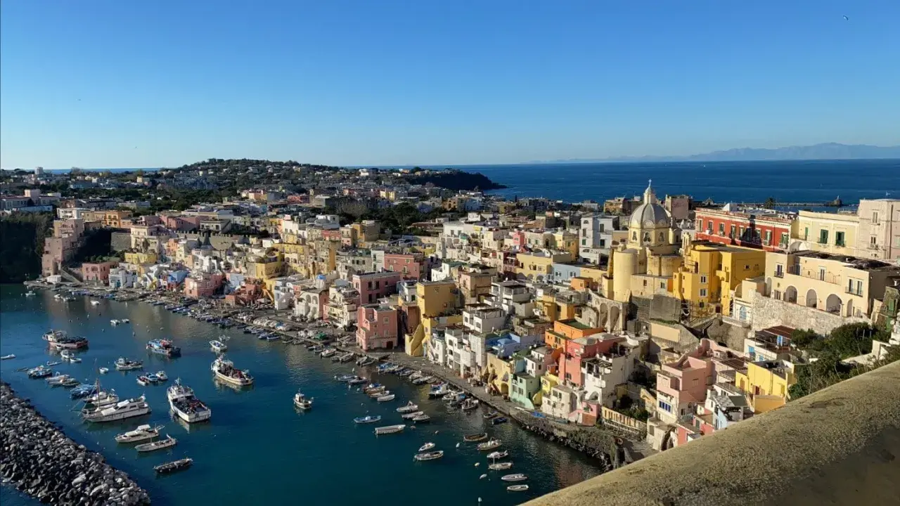 Vue panoramique de Procida ou Ischia, avec ses maisons colorées nichées sur la côte et des bateaux dans le port.
