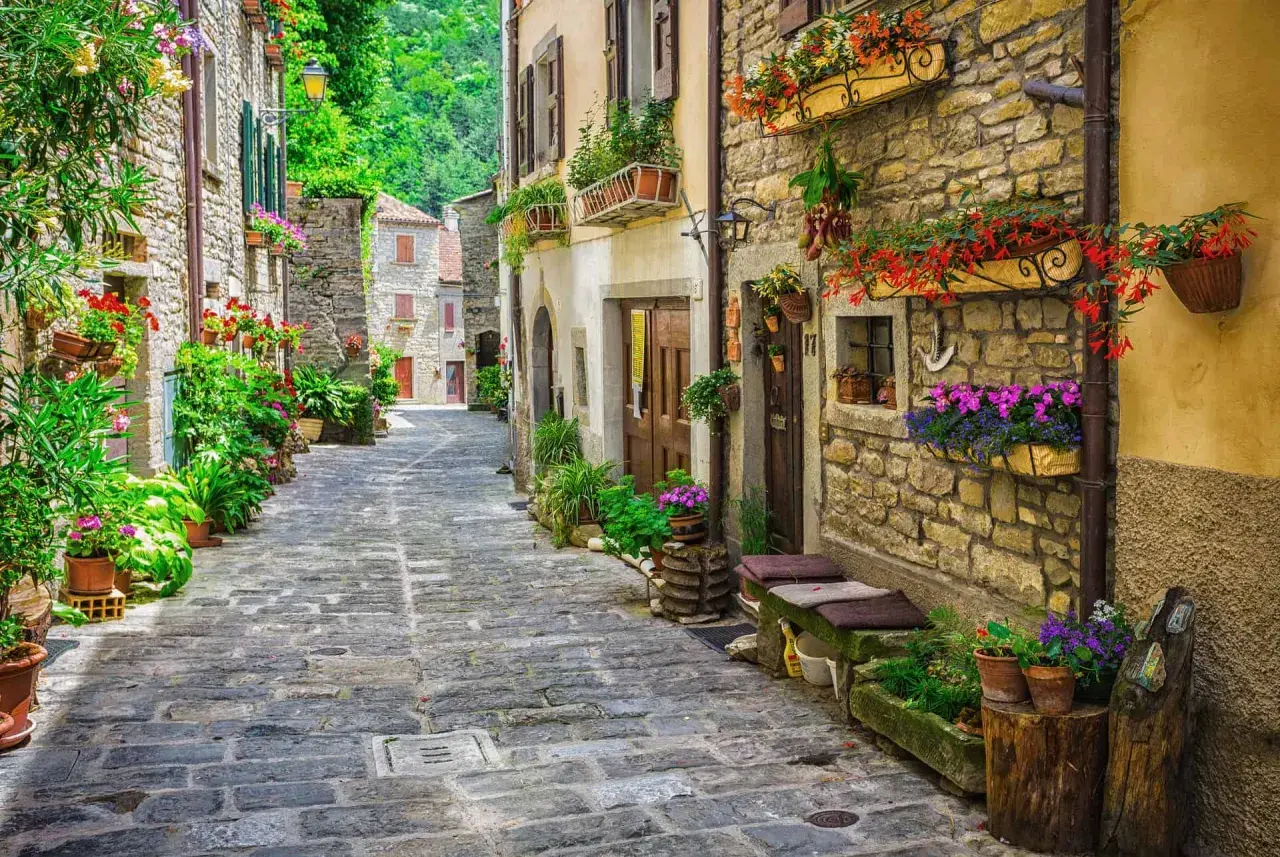 Ruelle pavée bordée de maisons en pierre ornées de fleurs colorées, évoquant une charmante résidence toscane.