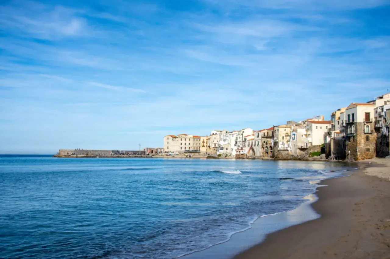 Vue de la plage et des maisons colorées de Cefalù, Sicile, sous un ciel bleu clair.