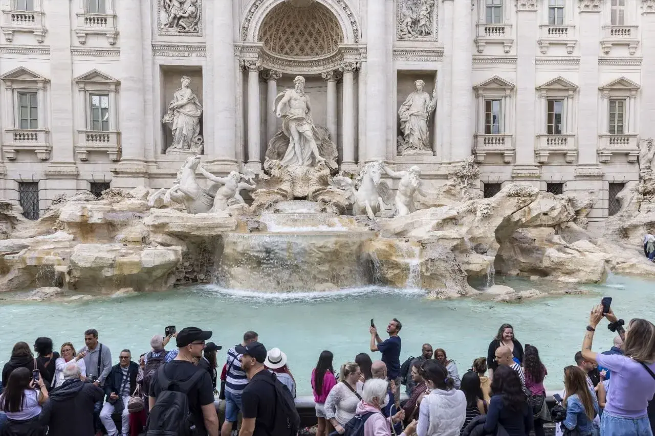 La fontaine de Trevi, avec ses statues majestueuses et ses chevaux marins, attire une foule de visiteurs capturant ce moment magique avec leurs téléphones.