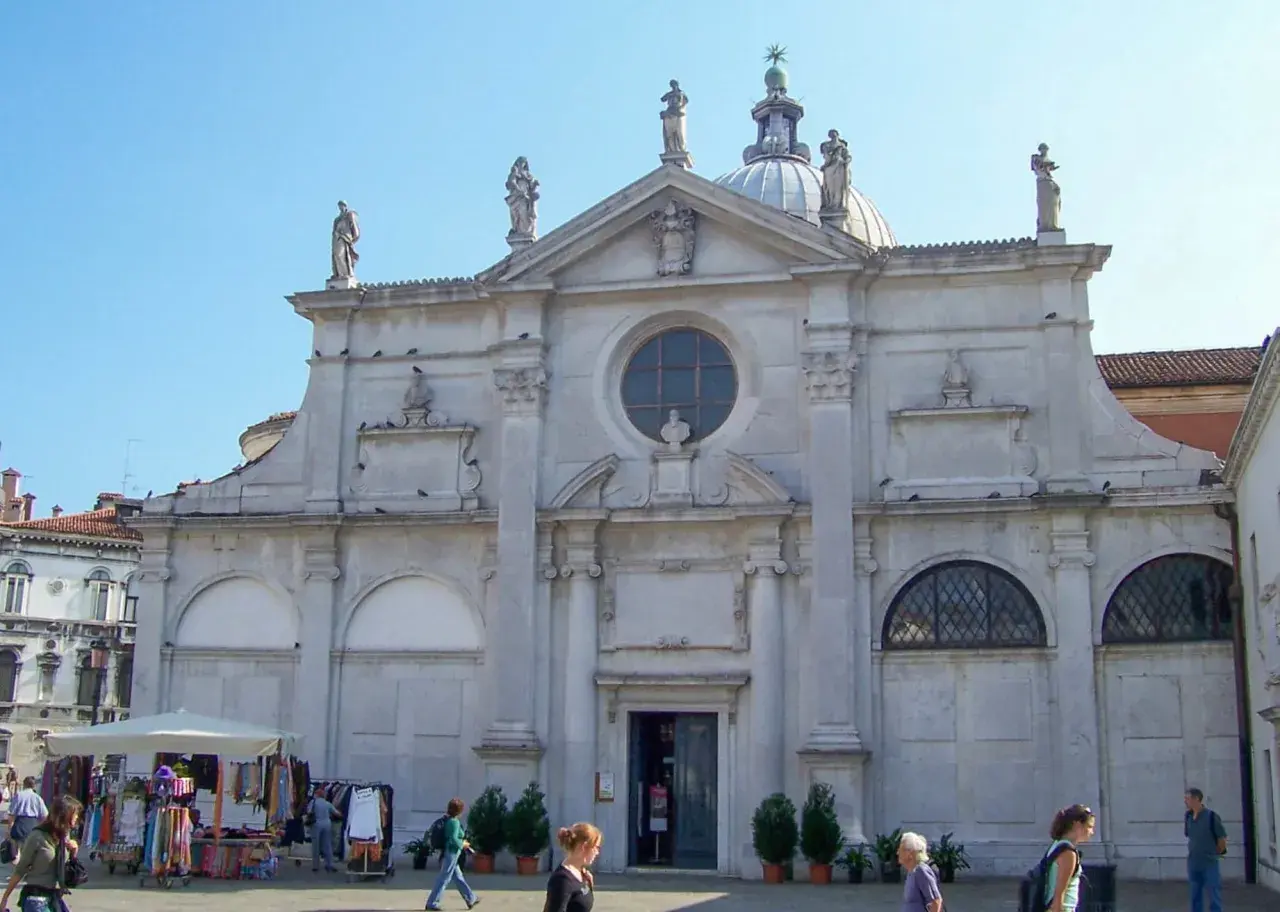 Façade de Santa Maria Formosa à Venise, avec des statues, un dôme et une place animée.
