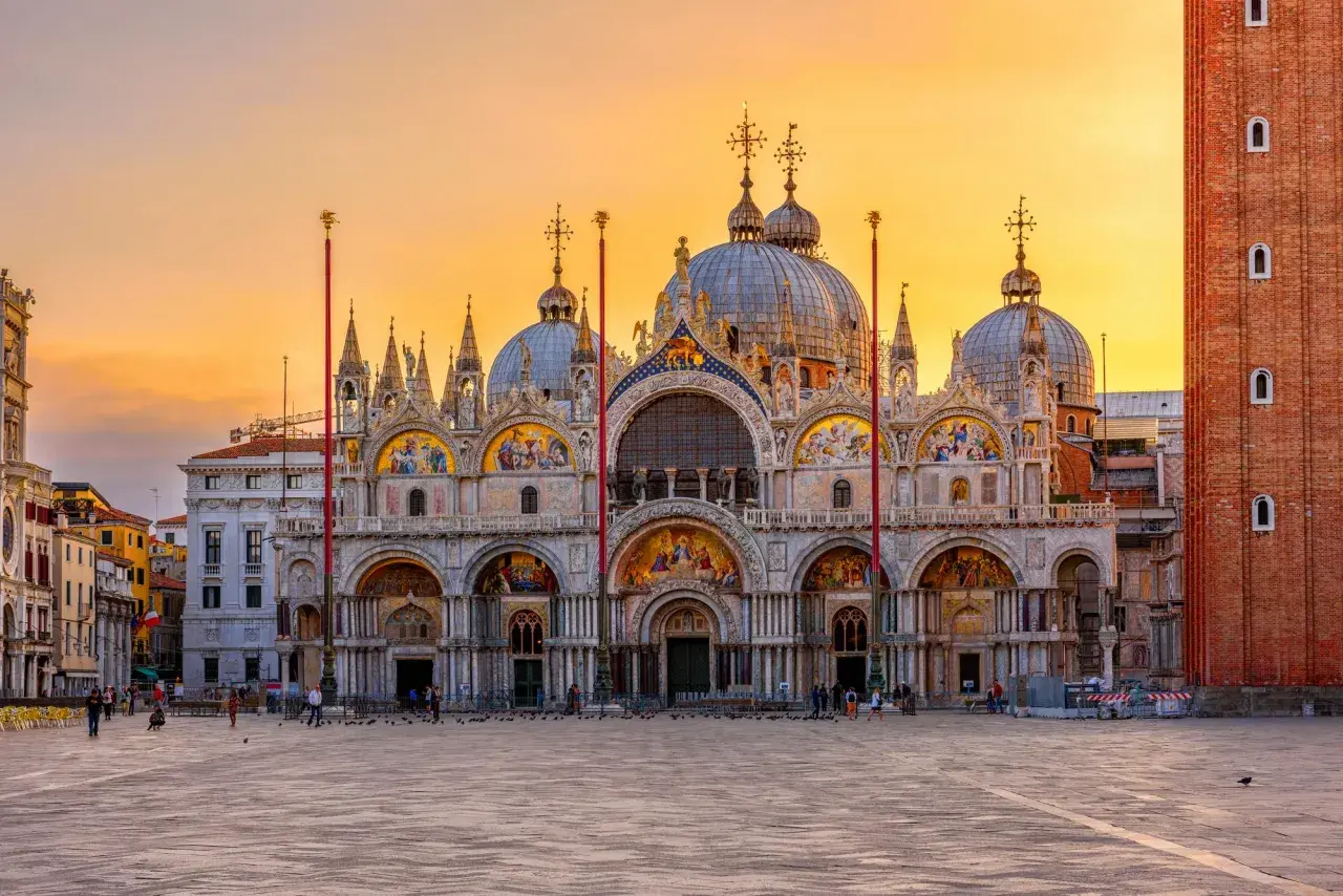 Magnifique coucher de soleil sur la place Saint-Marc, idéal pour visiter la basilique Saint-Marc. La façade ornée de mosaïques brille sous le ciel orangé.