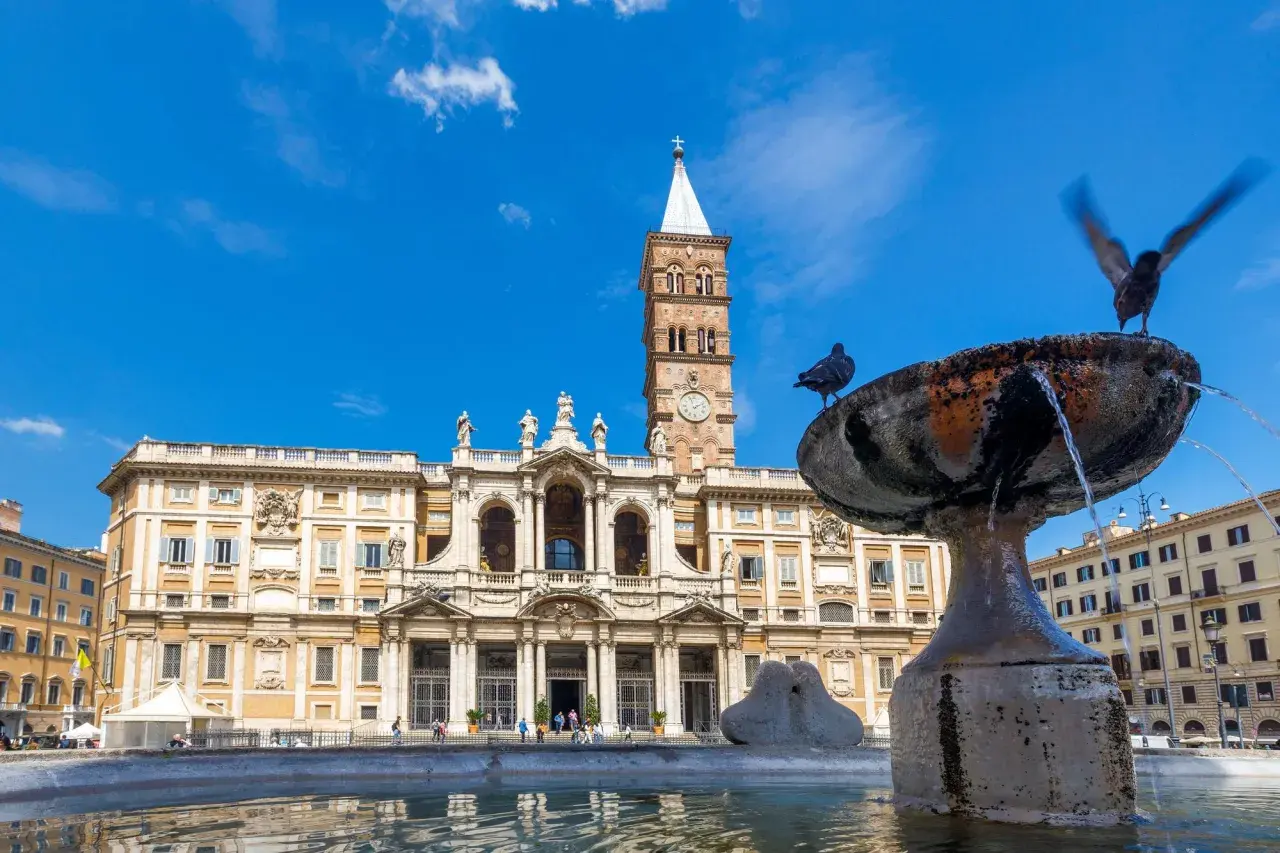 La basilique Sainte-Marie-Majeure se dresse fièrement sous un ciel bleu, avec une fontaine et des pigeons au premier plan.