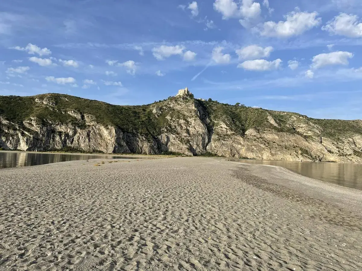 Plage de Patti, Sicile. Un château domine la colline rocheuse surplombant la mer calme et la plage de sable.