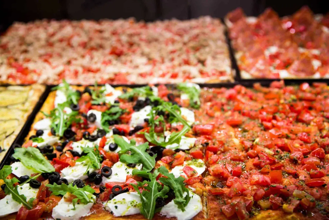 Des pizzas romaines rectangulaires appétissantes, dont une à la mozzarella fraîche, olives et roquette, la meilleure pizza Rome.