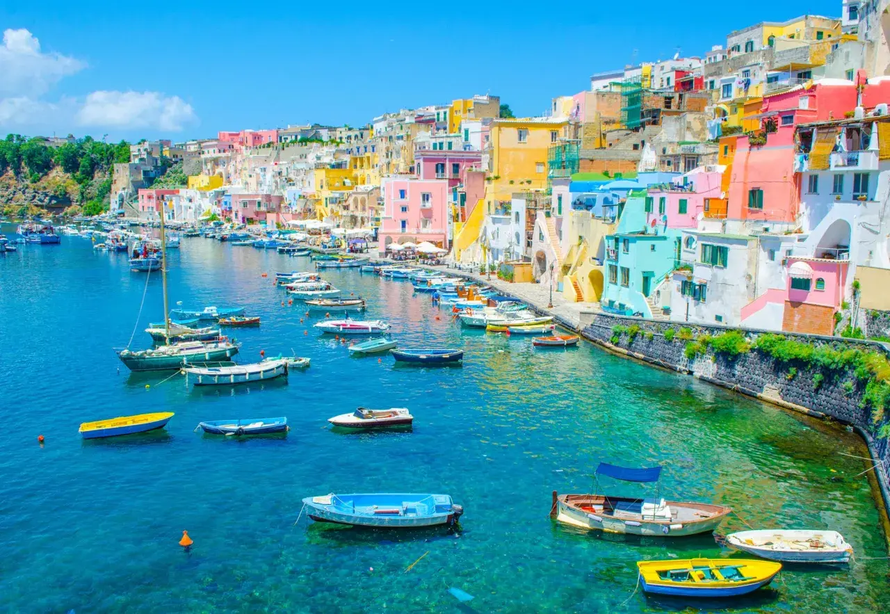 Un charmant port sur une île près de Naples, avec des maisons colorées et de nombreux bateaux dans l'eau turquoise.