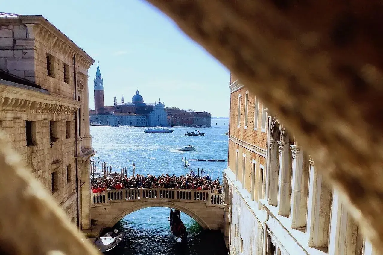 Vue d'un pont vénitien animé, avec des gondoles et des bateaux sur le canal, et des bâtiments historiques en arrière-plan.