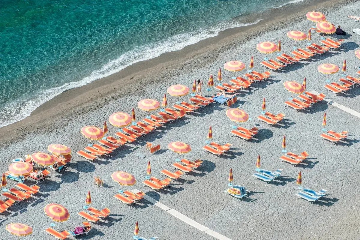 Lignes d'orange vif et de parasols colorés sur une plage de galets, une invitation à la détente. Destination Italie plage.