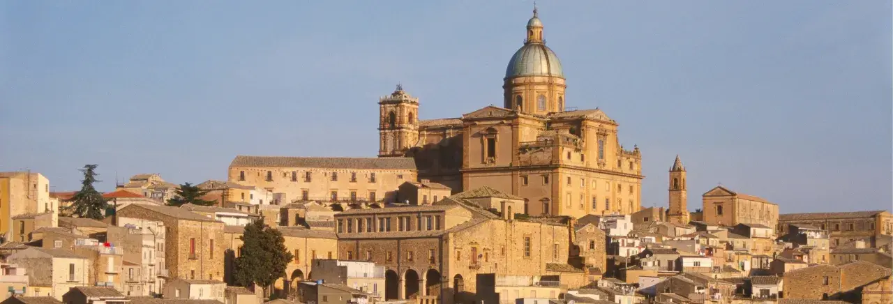 Vue panoramique de la ville de Piazza Armerina en Sicile, dominée par une imposante cathédrale à dôme vert.