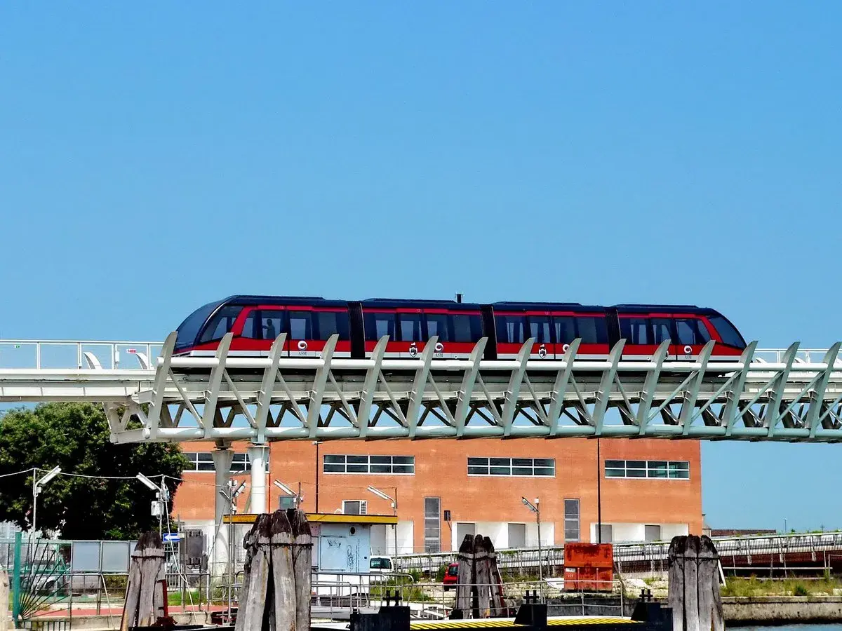 Le people mover de Venise, un train rouge et noir, circule sur une voie aérienne devant un bâtiment orange.