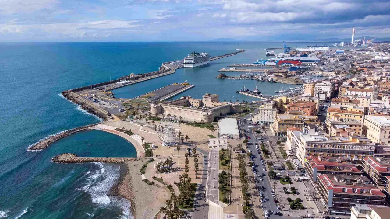 Vue aérienne du port de Civitavecchia, avec un immense paquebot de croisière, des bateaux, une forteresse historique et une grande roue.