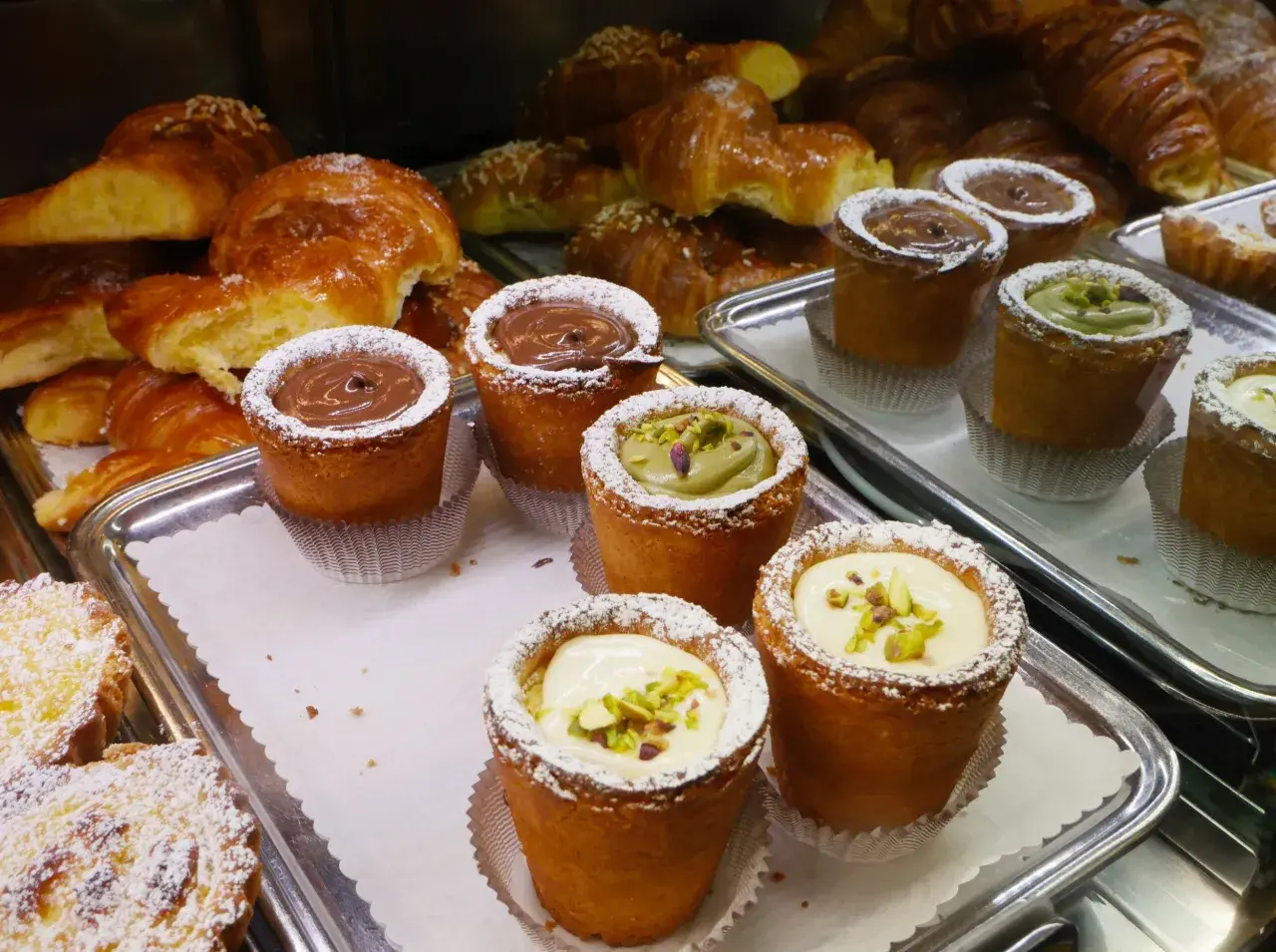 Pâtisseries variées, dont des croissants dorés et des petits gâteaux garnis de crème au chocolat, de pistache ou de crème pâtissière, dans un restaurant florentin.