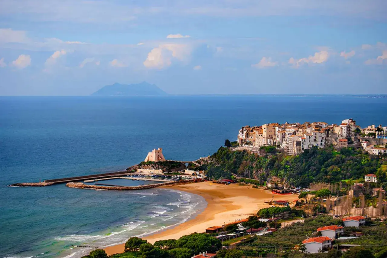 Vue d'un village pittoresque perché sur une falaise surplombant la mer, avec une plage de sable et un port. On dirait un **ostie** de **Rome** !