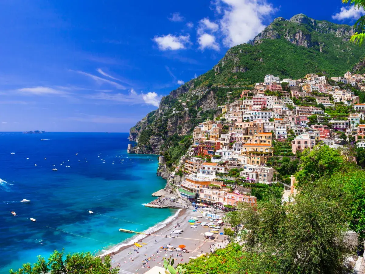 Vue spectaculaire de Positano, une ville pittoresque perchée sur une falaise en **Agerola, Italie**. Les maisons colorées descendent vers une plage animée et la mer d'un bleu profond.