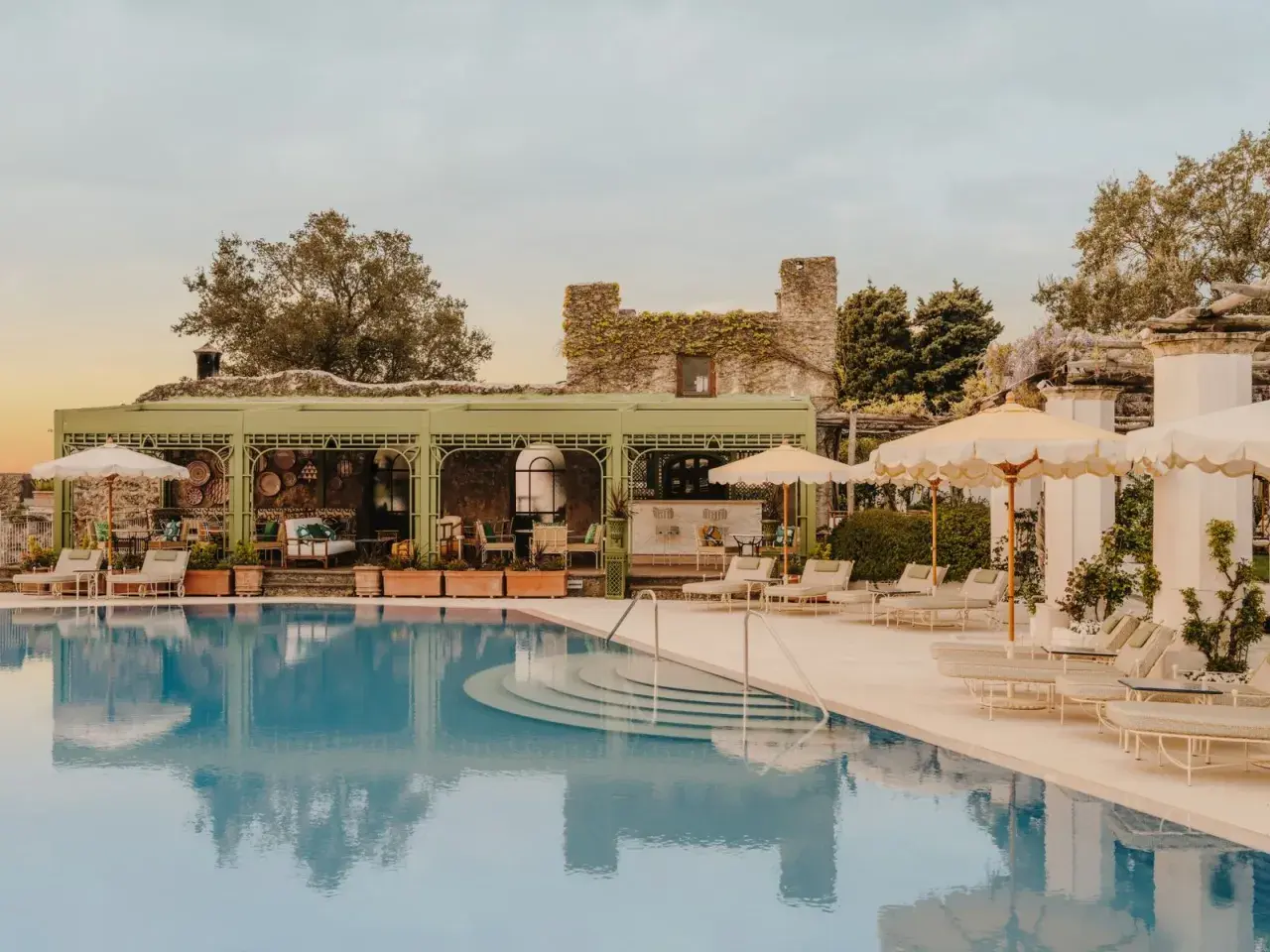 Piscine d'un hôtel club sur la côte amalfitaine, avec des chaises longues, des parasols et un bar extérieur.