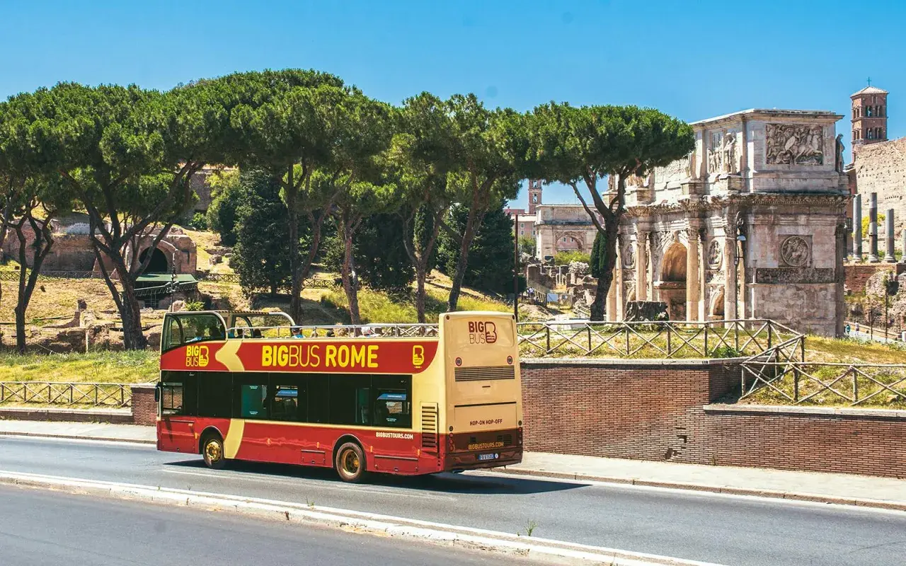 Un bus touristique rouge et jaune circule près de l'Arc de Constantin. Le Vatican n'est pas loin, offrant une vue sur Rome.